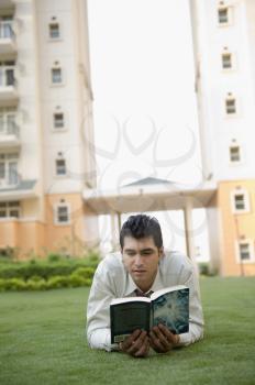 Businessman lying on the grass and reading a book