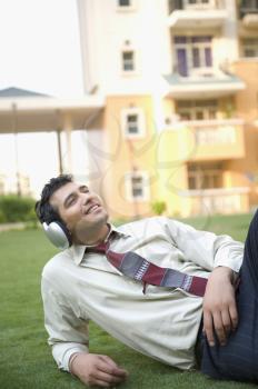Businessman lying on the grass and listening to music