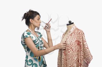 Female fashion designer trying a dress on a mannequin and drinking water
