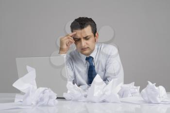 Businessman looking worried with crumpled papers on desk