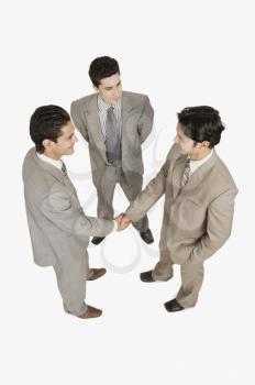 Two businessmen shaking hands with another businessman standing beside them