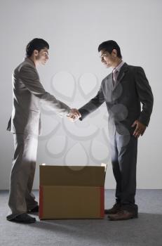 Two businessmen shaking hands over an illuminated cardboard box