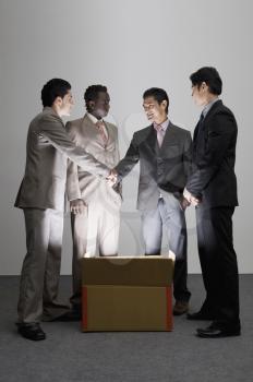 Two businessmen shaking hands over an illuminated cardboard box with their colleagues standing beside them