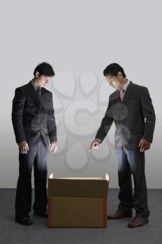 Two businessmen looking into an illuminated cardboard box