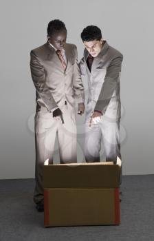 Two businessmen looking into an illuminated cardboard box