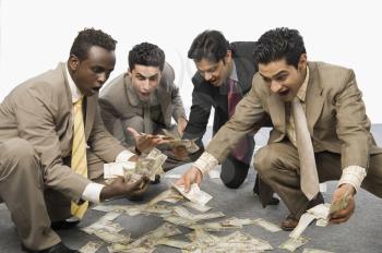 Four businessmen crouching and holding currency notes