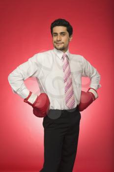 Portrait of a businessman wearing boxing gloves and standing with arms akimbo