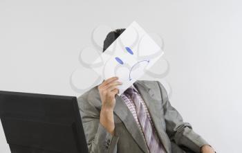 Businessman holding a smiley face paper in front of his face