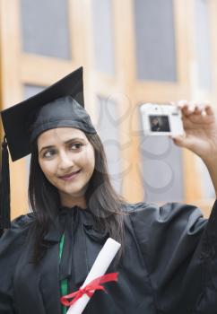 Woman in graduation gown taking a picture of herself with a digital camera