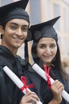 Couple in graduation gowns holding diplomas and smiling