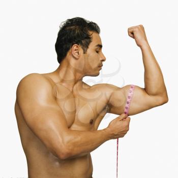 Close-up of a man measuring his biceps with a tape measure