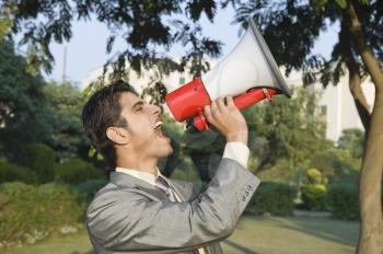 Businessman shouting into a megaphone in a park