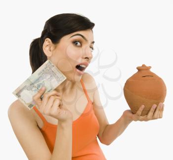 Woman holding Indian currency notes with a piggy bank