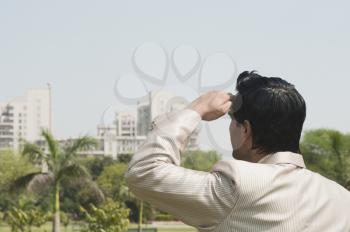 Businessman looking towards a city with shielding eyes