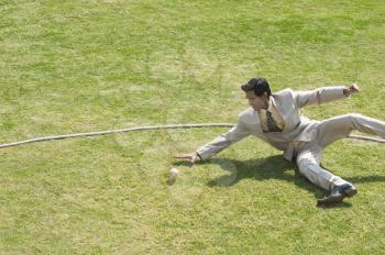 Businessman diving to stop a ball near boundary line in a cricket field