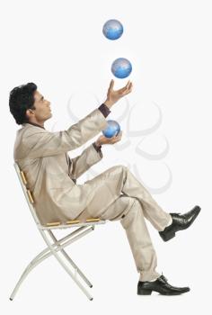 Businessman sitting on a chair and juggling with globes