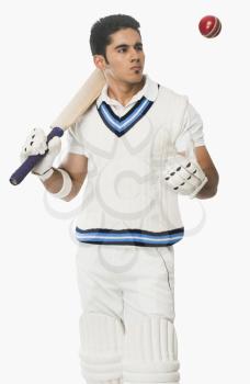 Cricket batsman holding a bat and looking at a ball