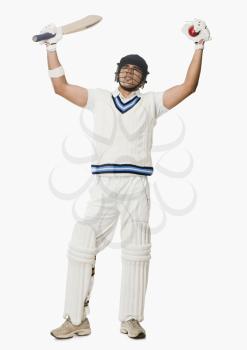 Cricket batsman holding a ball and bat with his arms raised