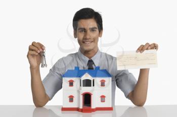 Real estate agent showing keys and a check near a model home
