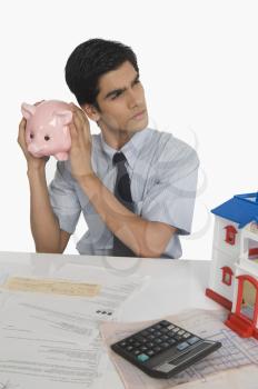 Real estate agent holding a piggy bank near his ear