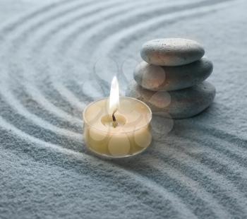 light warm candle and cool stone on sand 