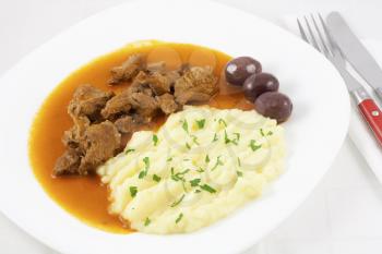 Beef goulash with mashed potato spiced with parsley and three brown olives.