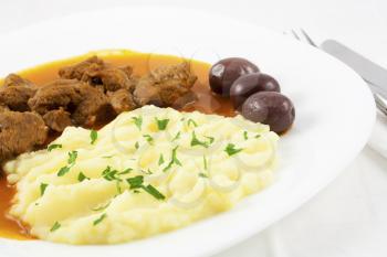 Goulash with mashed potato spiced with parsley and three brown olives.