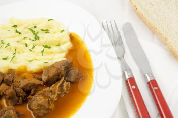 Delicious goulash with mashed potato spiced with parsley and slice of bread.