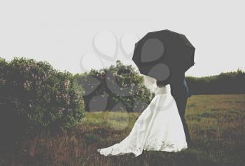 Photo of bride and groom under black umbrella at park