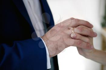 hands of a bride and a groom, woman putting a wedding ring on the finger of her groom