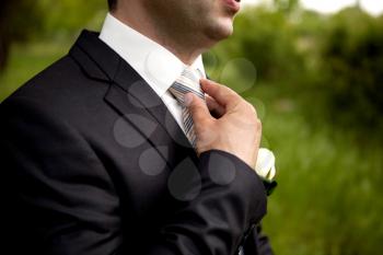 The groom in a suit, corrects a tie with his hand. Close-up composition