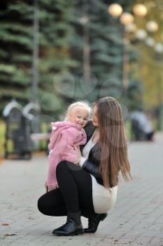 A young mother in a sweater hugs her cute blonde daughter during a walk in the autumn Park, against the background of the alley