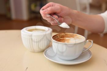 The girl's hand pours sugar into her coffee.