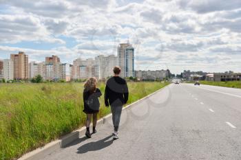 Teenagers walk along the highway and reach the city.
