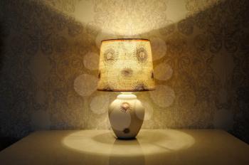A small table lamp, with a yellow light on the bedside table
