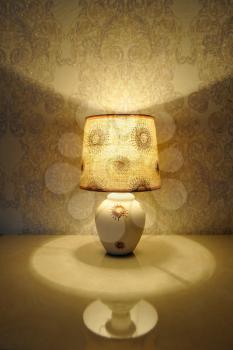 A small table lamp, with a yellow light on the bedside table