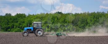 A blue tractor plows the field in the spring.