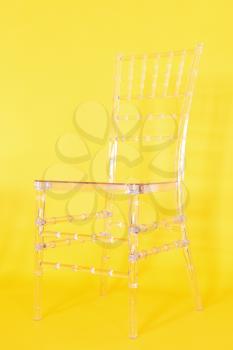 Transparent plastic chair on a yellow background in a photo studio.