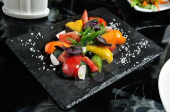 Sliced vegetables on a wooden board in a restaurant, cucumbers, tomatoes, peppers, lettuce leaves.