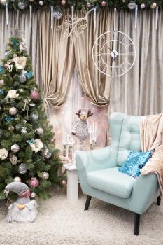 Home Christmas interior with a Christmas tree and a light armchair, against the background of a window with a curtain