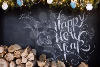 Beautiful inscription on a chalkboard, happy new year, decor and firewood for a fireplace.