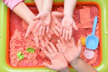 Children play with pink kinetic sand for sculpting figures. Top view