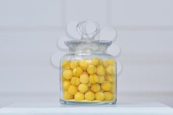 beautiful fresh yellow sugar dragees are stored in a glass transparent jar against the background of the white wall
