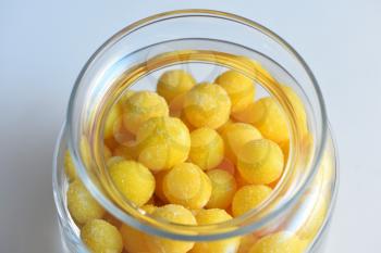 beautiful fresh yellow sugar dragees are stored in a glass transparent jar on the white background. Close-up