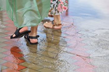 Two girls walk along the sidewalk of a tile after a heavy rain on the water in summer shoes, in sandals, their feet were soaked.