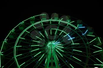 Glowing ferris wheel in an amusement park against a black night sky.