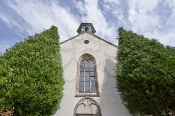 Beautiful and old Christian church with a cross and 2 big thujas in the European city of Baden Baden