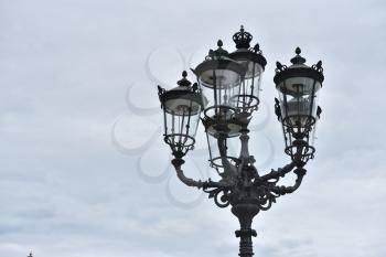 Beautiful classic iron lamppost of six lamps with diode bulbs against a cloudy sky