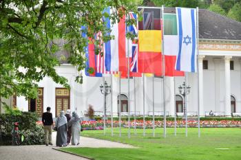 A group of refugees from the Middle East, three women in hijabs and a man walking in the park in Europe, against the background of the flags of the countries of the European Union, America, England