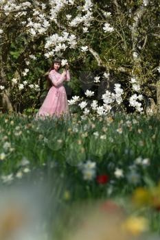 A young girl in a lush pink dress next to a large and blooming magnolia tree. Girl and tree with white magnolia flowers